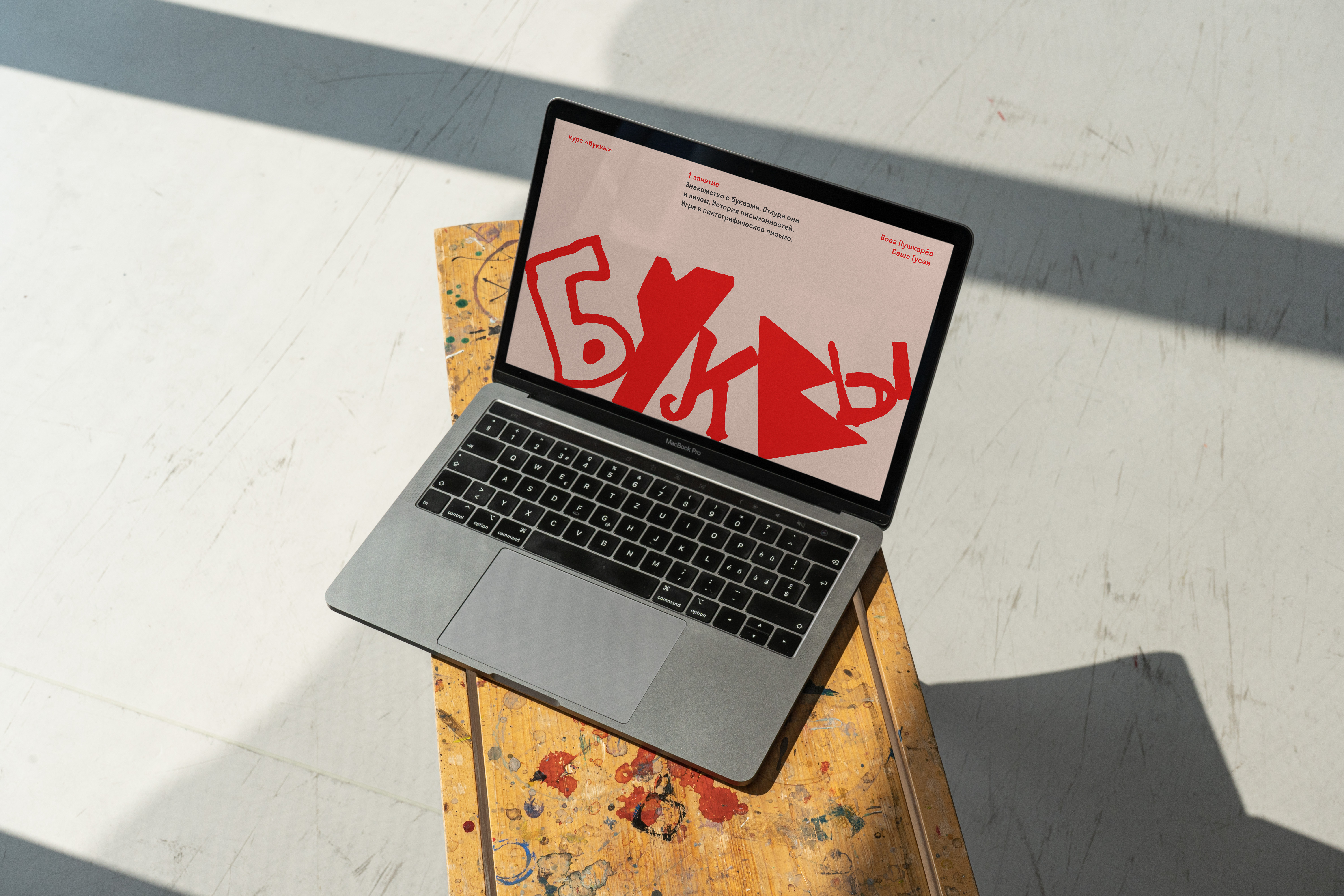 Laptop on a stool showing a Mezhdu Prochim slide with large red Cyrillic letterforms